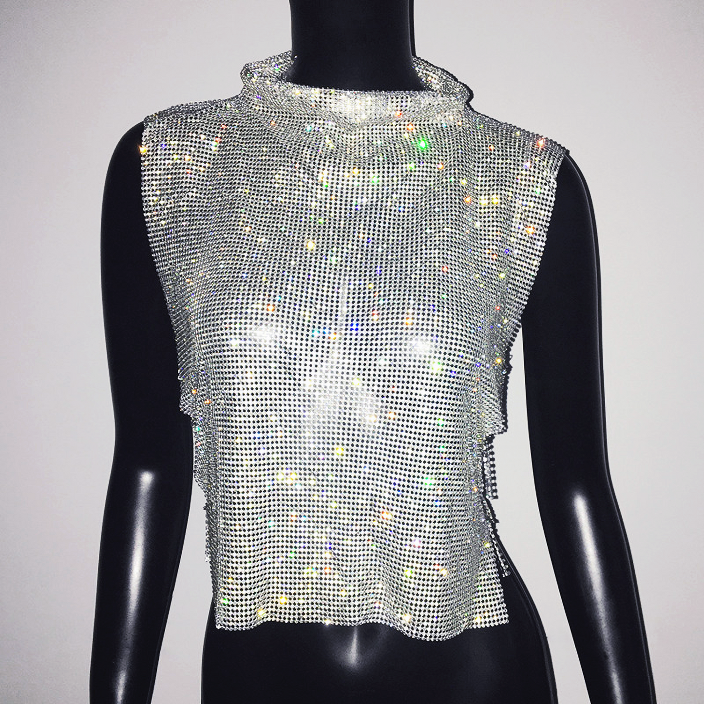 A woman wearing a sleeveless chain mail crop top with a high neck and rhinestone embellishments.
