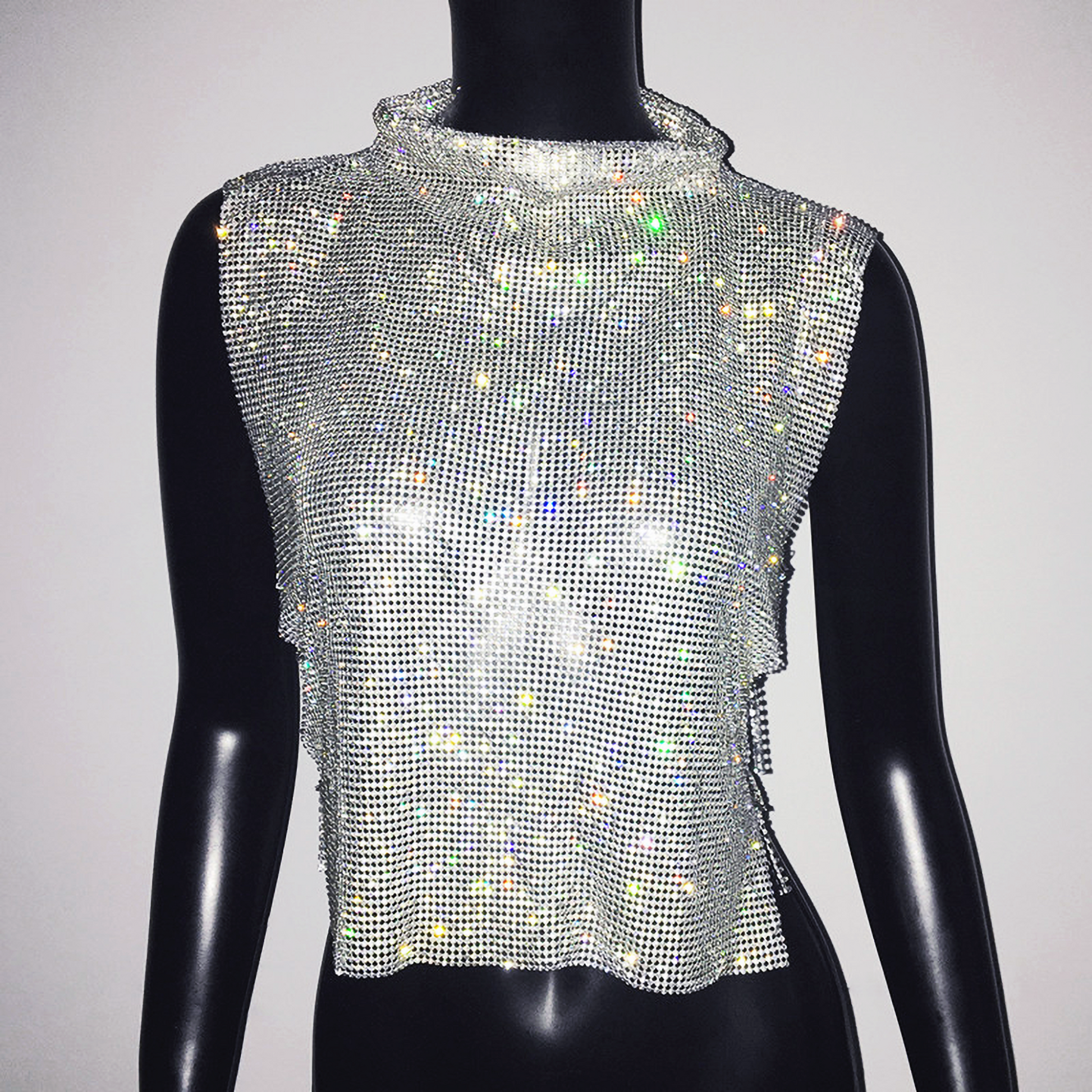 A woman wearing a sleeveless chain mail crop top with a high neck and rhinestone embellishments.